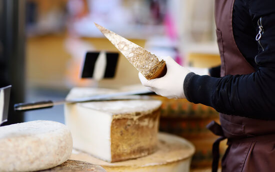 Seller cutting organic cheese on farmer market in Strasbourg, France